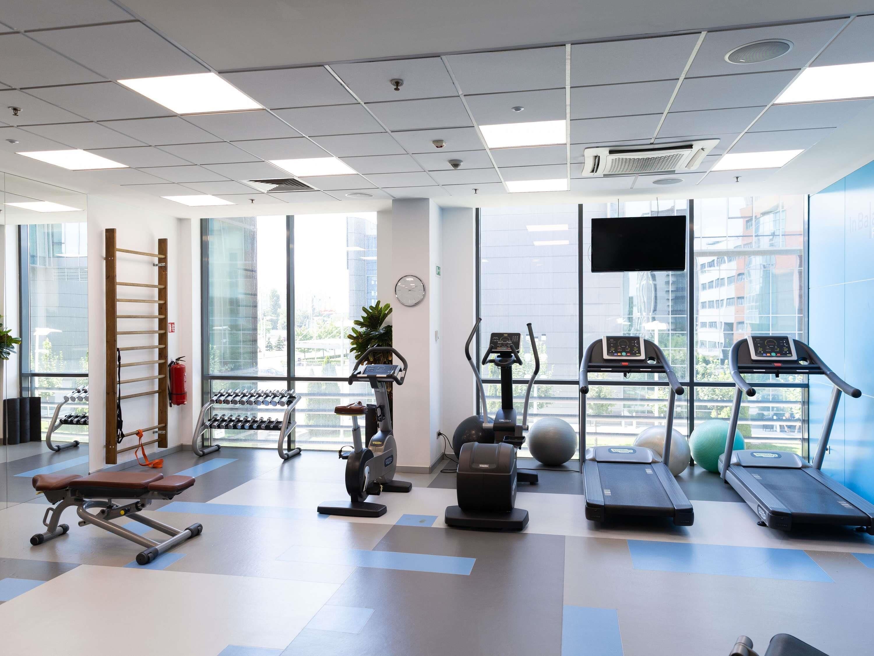 Un gimnasio con equipo de ejercicio, una banca, una cinta de correr y ventanas amplias.