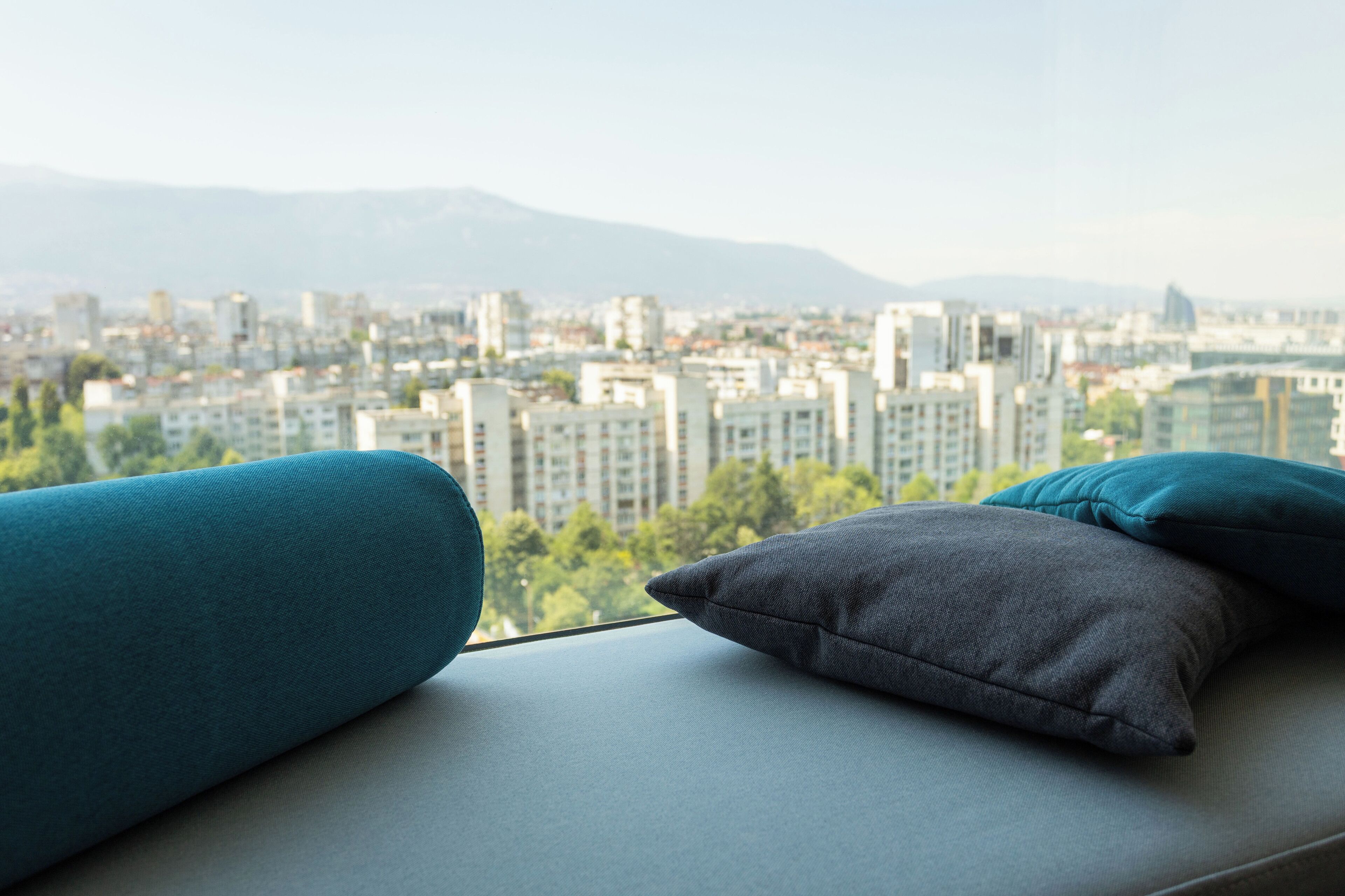 A cityscape view from a window with a sofa and cushions.