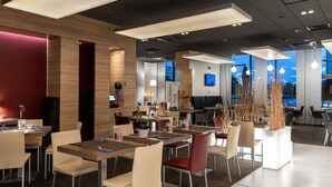 A modern restaurant interior with high ceilings, pendant lighting, and a mix of seating arrangements. - Novotel Sofia (Sofia)