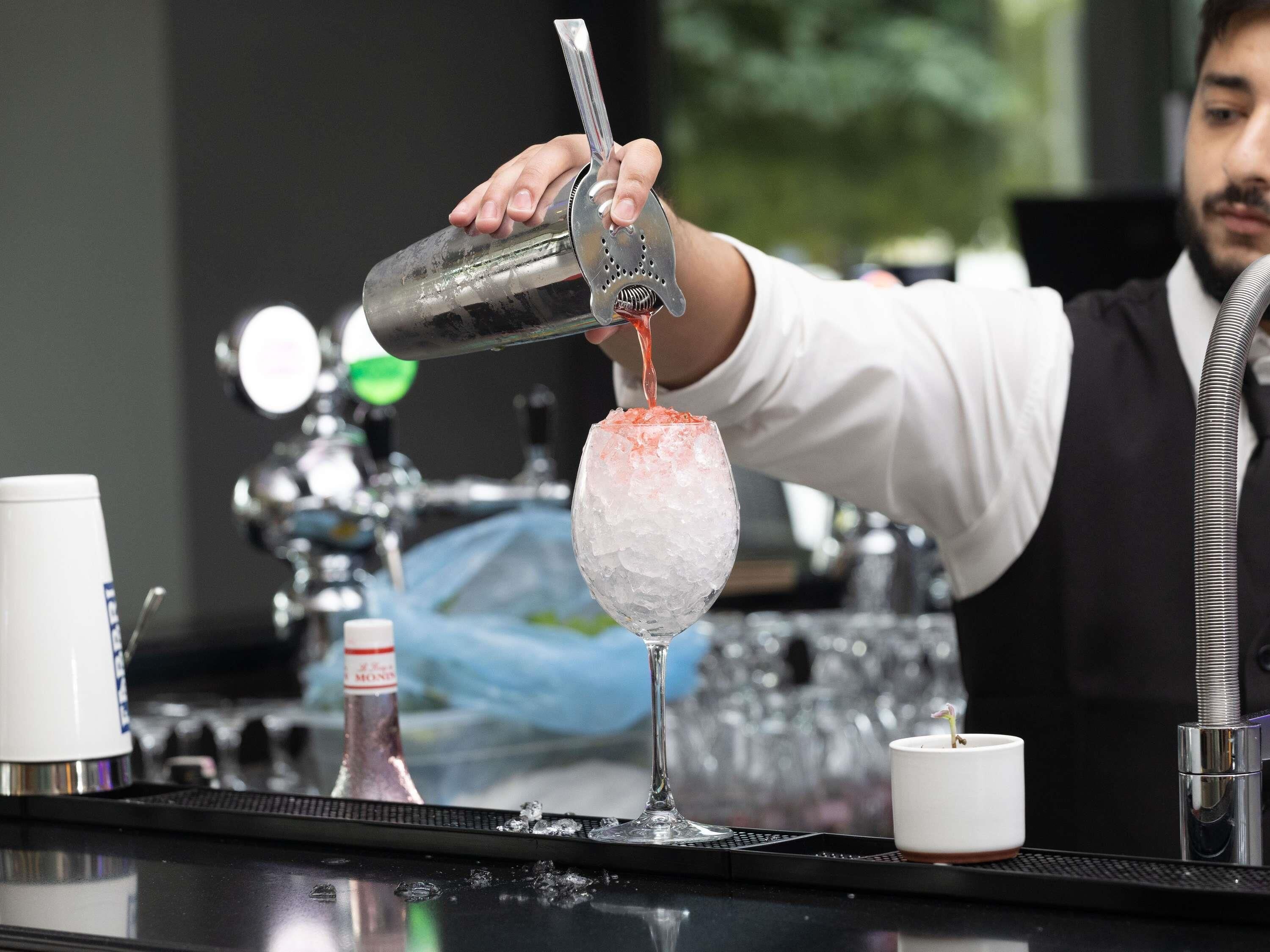 A bartender pouring a drink into a glass with ice.