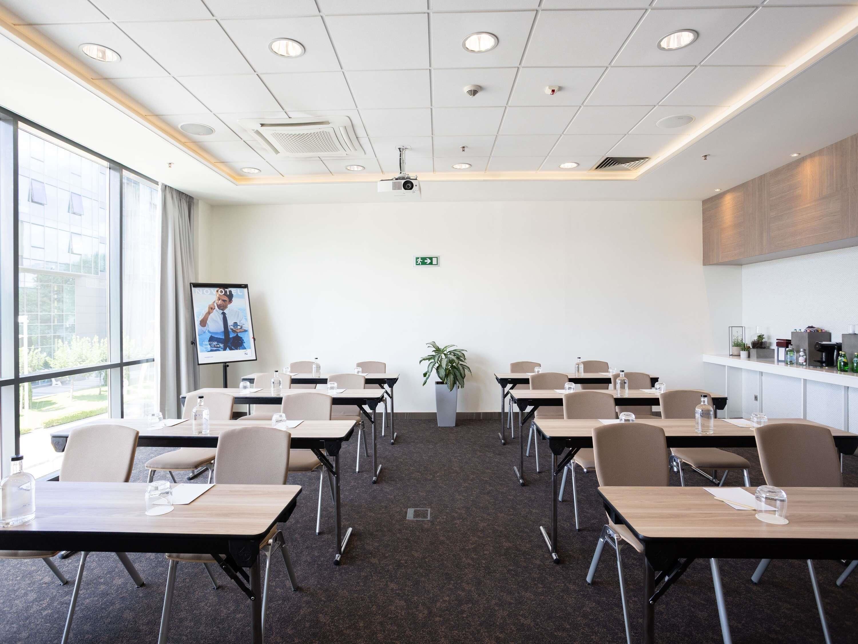 A conference room with tables, chairs, a projector, and a large window.