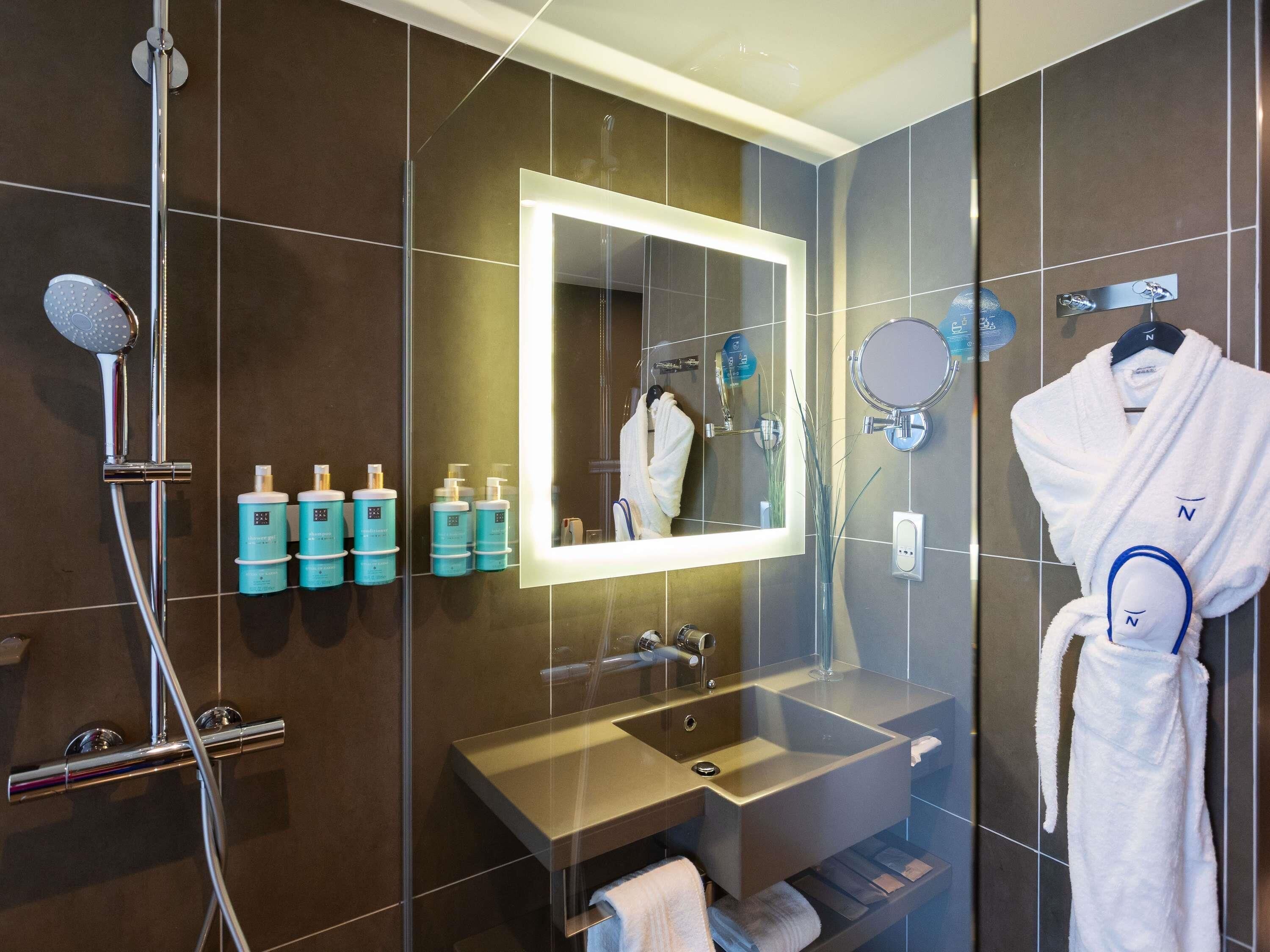 A modern bathroom with a glass shower enclosure, a vanity with a sink, a mirror, and toiletries.