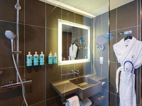 A modern bathroom with a glass shower enclosure, a vanity with a sink, a mirror, and toiletries.