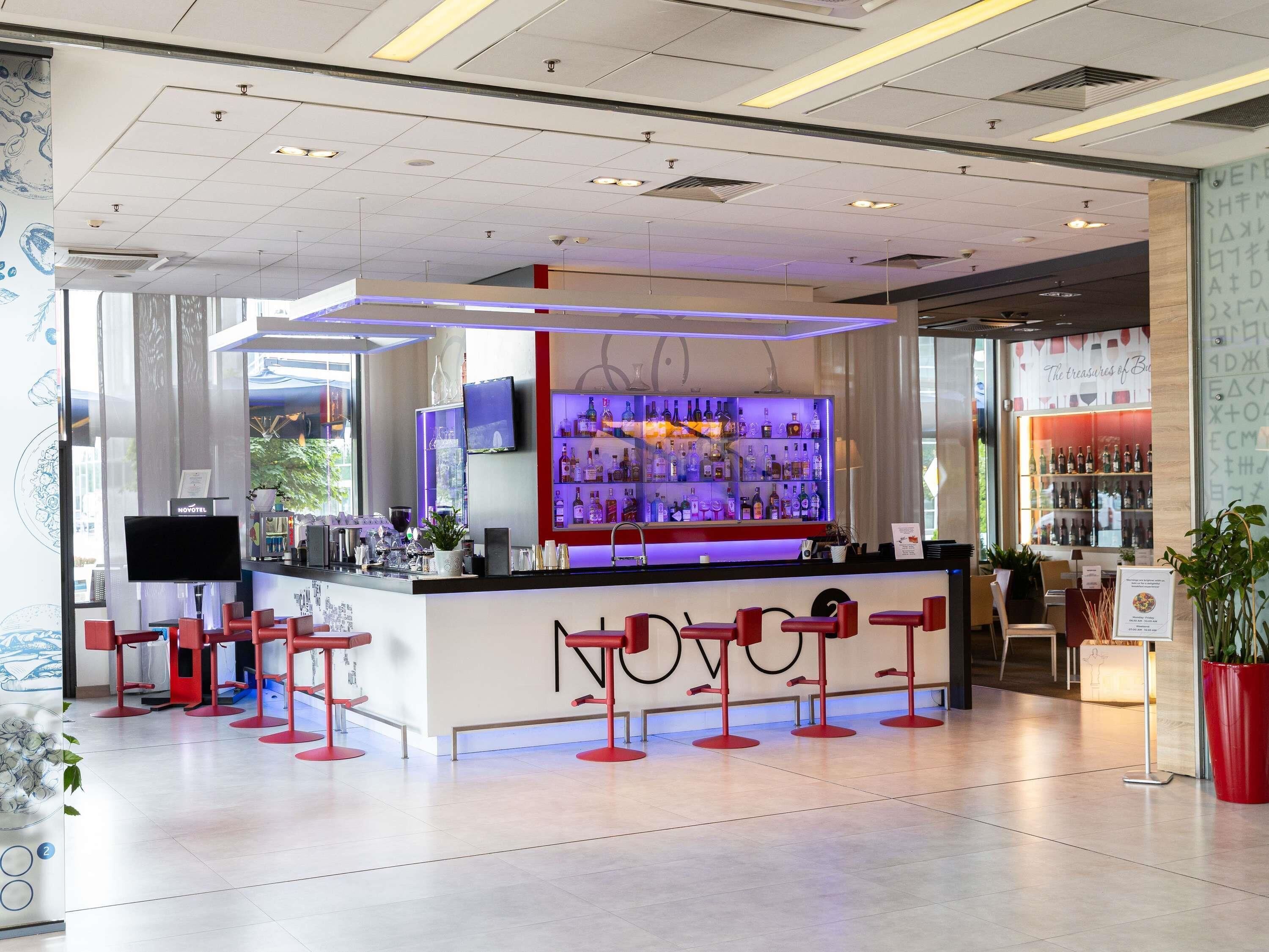 A modern bar area with a counter, red stools, and a television screen.