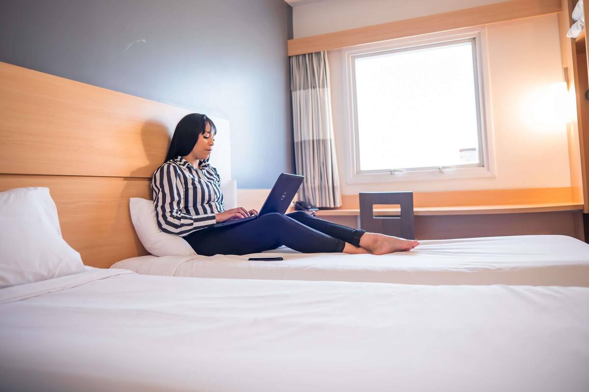 Ein Hotelzimmer mit Bett, Laptop und einem Vorhangfenster.