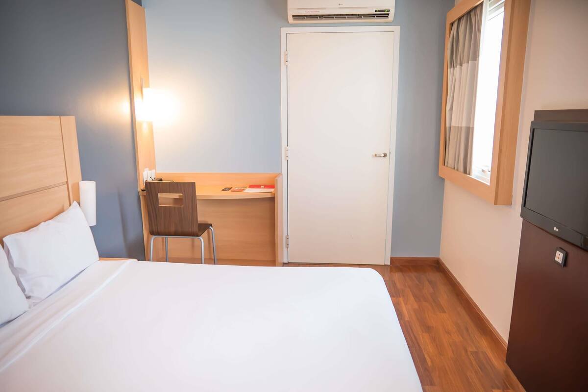 Ein Hotelzimmer mit Bett, Schreibtisch, Stuhl, Klimaanlage und Fernseher.