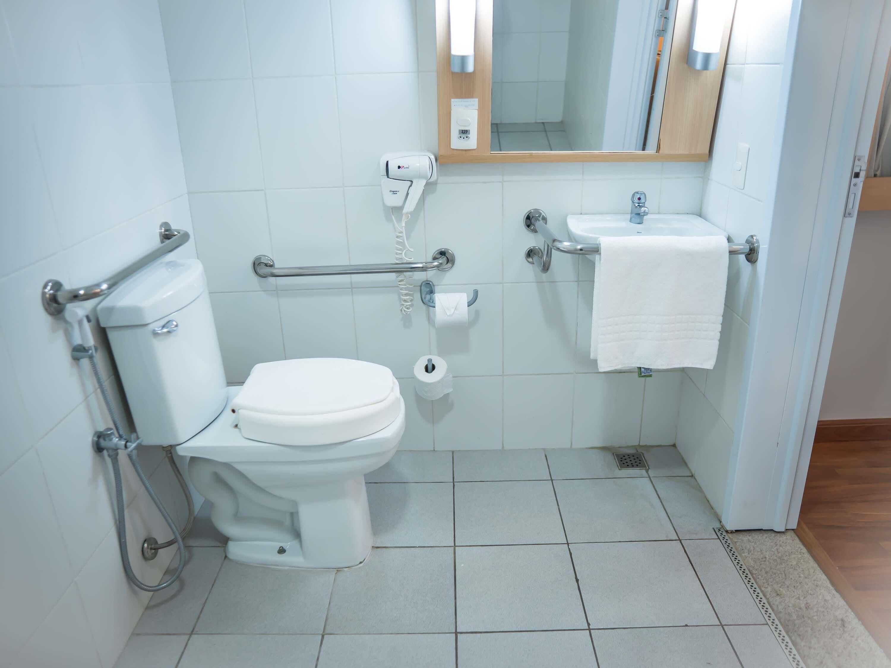 A bathroom with a toilet, bidet, hand dryer, and a sink with a towel.