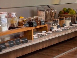 A breakfast buffet with labeled containers of food and plates for guests. - ibis Itu Plaza Shopping Hotel (Itu)