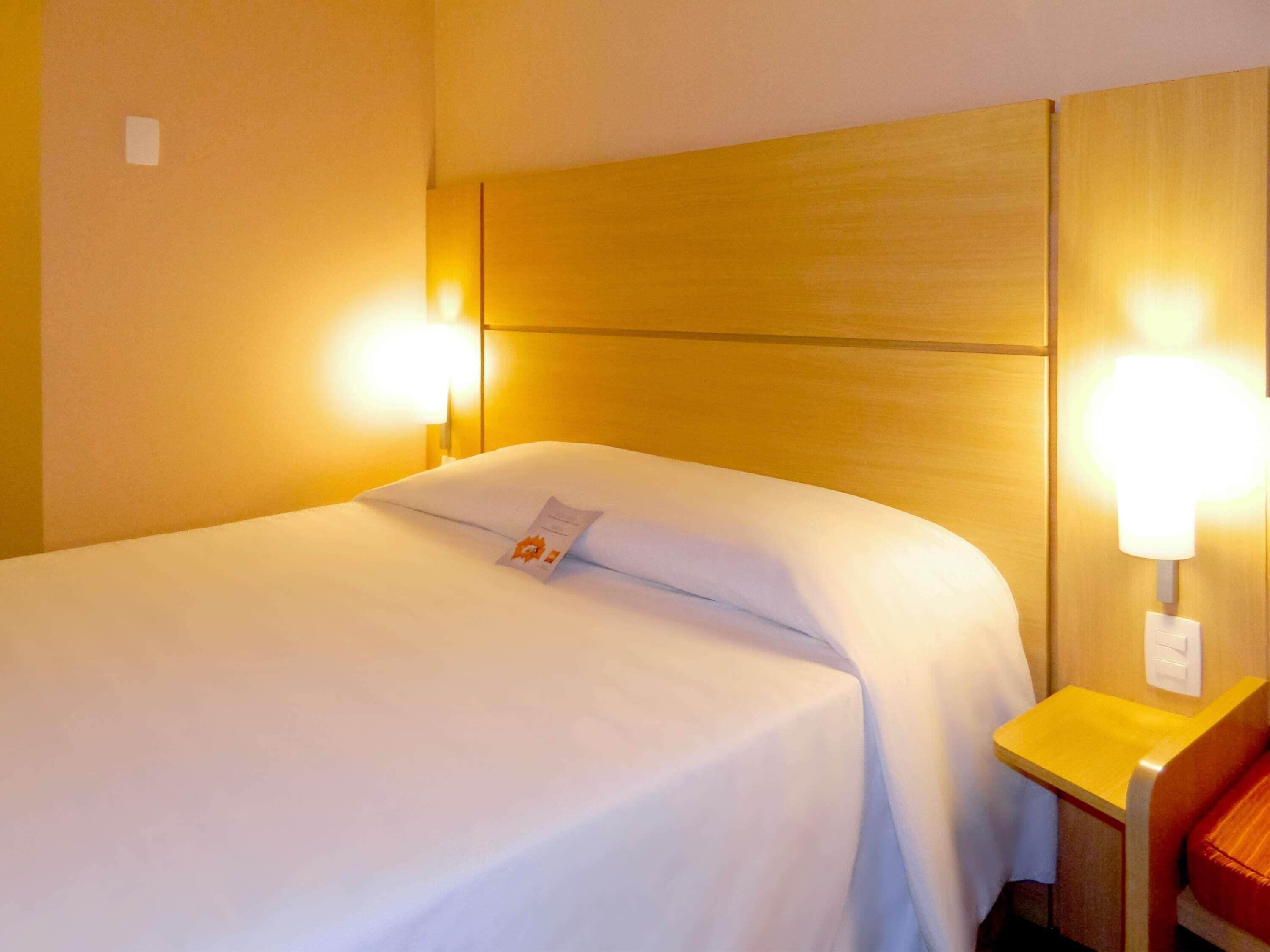 A hotel room with a bed, two bedside lamps, and a wooden headboard.