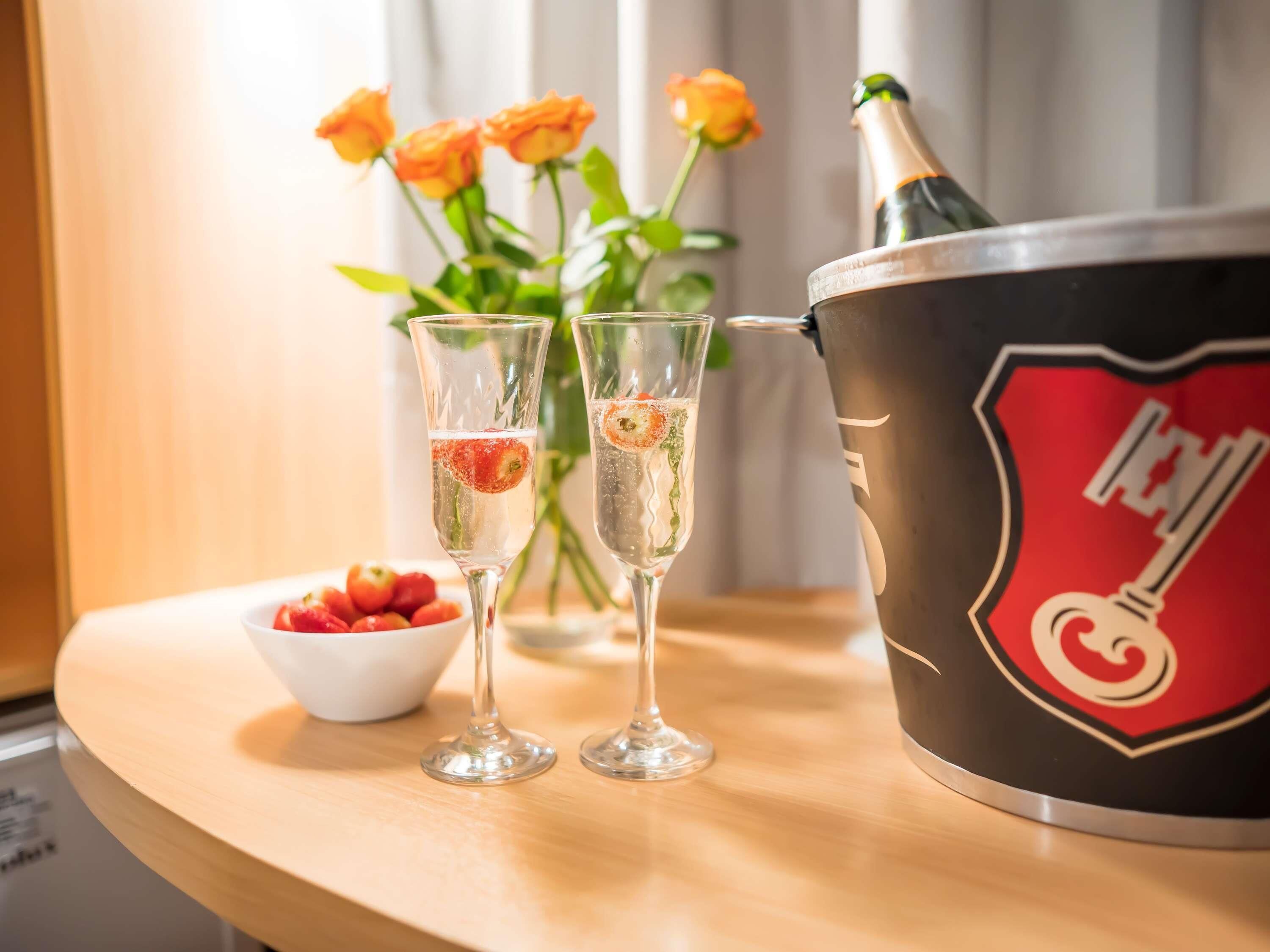 Deux flûtes à champagne décorées de fruits, un seau à champagne et un saladier de fraises sur une table en bois.