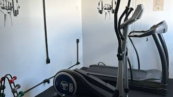 Un gimnasio en casa con una bicicleta estática, una elíptica y un banco de pesas.