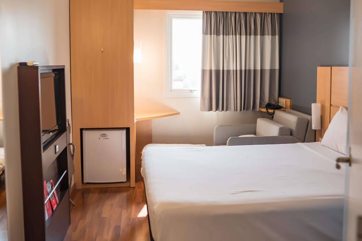 Ein Hotelzimmer mit Bett, Schreibtisch, Stuhl, Fernseher und einem kleinen Kühlschrank.