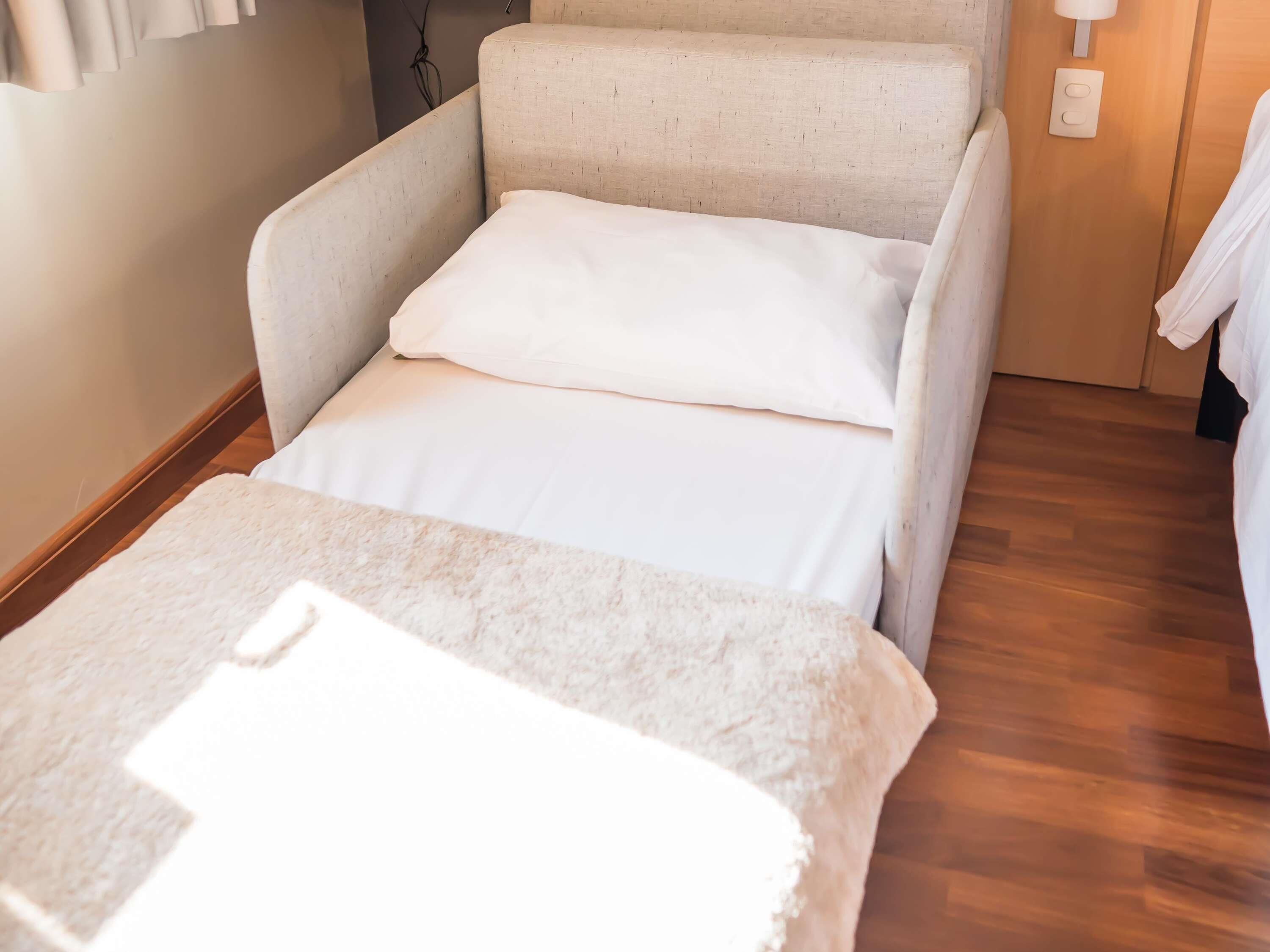 A small, cozy room with a single bed, a chair, and a wooden floor.