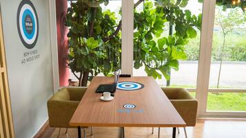A conference room with a wooden table, two chairs, a laptop, a cup, and a large window with a view of greenery.