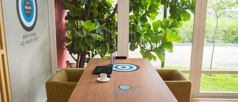 A conference room with a wooden table, two chairs, a laptop, a cup, and a large window with a view of greenery.
