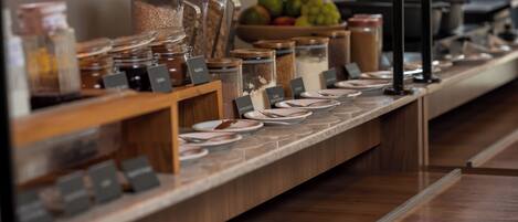 Montaje de buffet con diferentes alimentos y condimentos en recipientes de vidrio, identificados con sus nombres.
