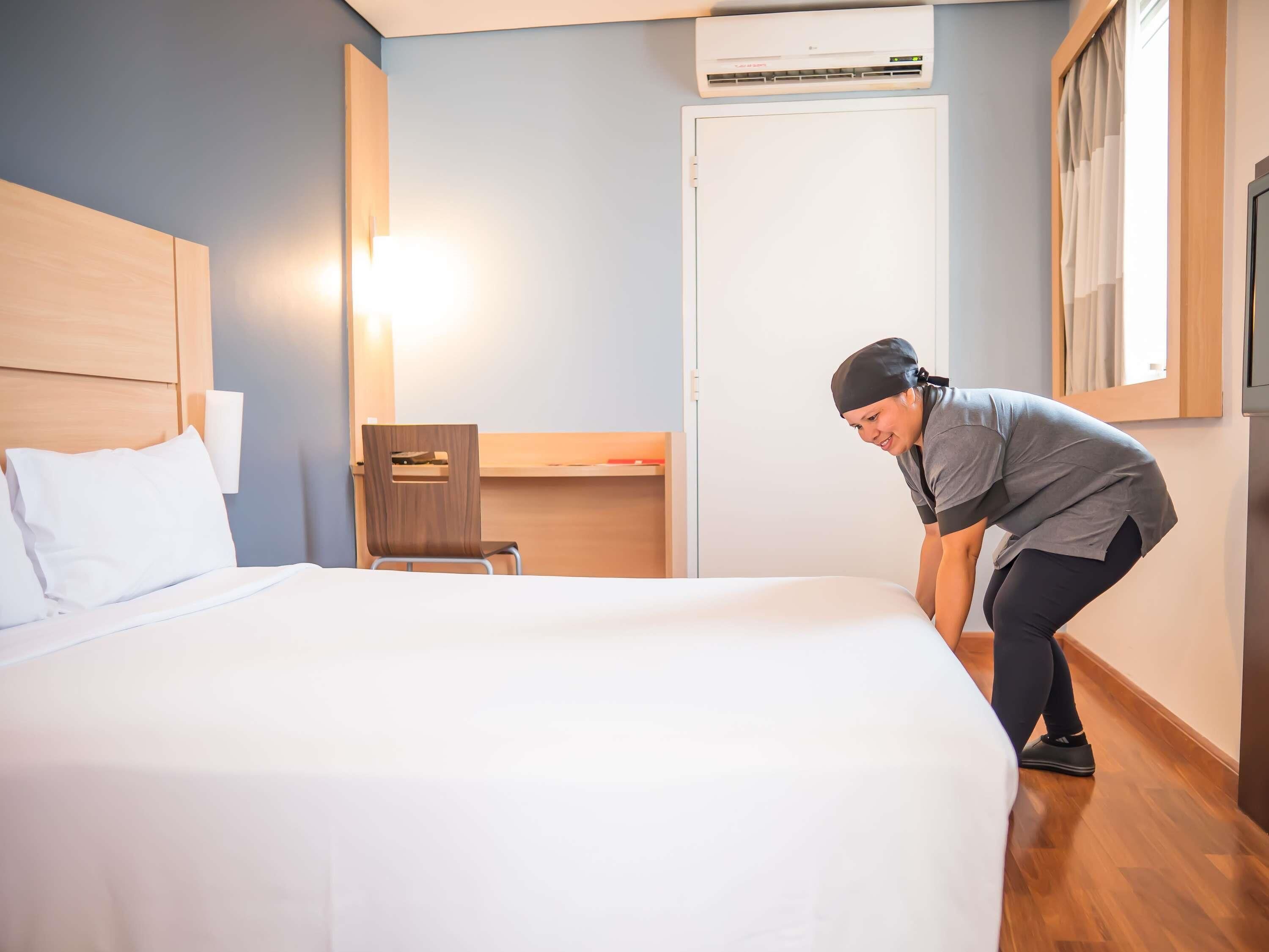 Habitación de hotel con cama, escritorio, silla, aire acondicionado y ventana con cortinas.