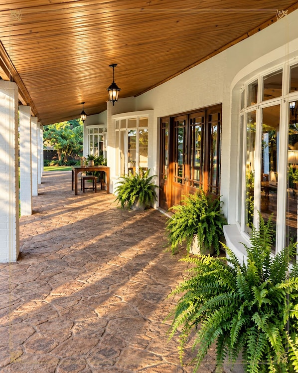 Un patio cubierto con suelo de piedra, techo de madera y ventanas amplias.