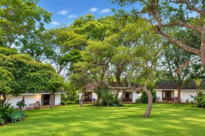 A bungalow-style property with a well-maintained lawn, multiple trees, and a clear sky. - Musketeers Lodge (Bulawayo)