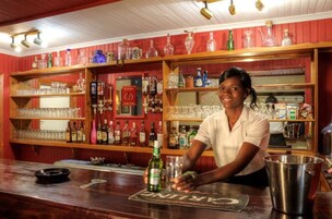 A bar area with shelves of liquor bottles and glasses, a bartender preparing a drink, and a cash register.