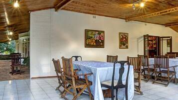 A dining area with wooden tables and chairs, white walls, and ceiling beams.