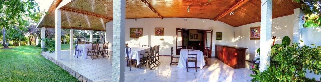 Un espace extérieur aménagé en terrasse, avec des tables et des chaises, un comptoir d’accueil et un coin salon abrité.