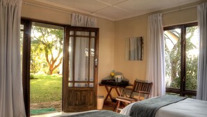 A room with two beds, a desk with a chair, a window, and a door leading to an outdoor area. - Musketeers Lodge (Bulawayo)