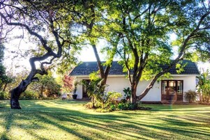 A house with a sloped roof, surrounded by a well-maintained lawn and large trees.