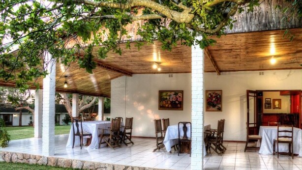An outdoor covered patio with tables and chairs, stone walls, and a wooden ceiling. - Musketeers Lodge (Bulawayo)