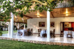 Un patio techado al aire libre con mesas y sillas, muros de piedra y techo de madera.