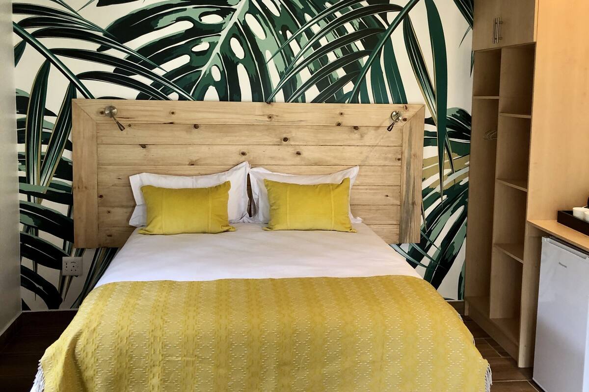 Un lit avec une tête de lit en bois, une couvre-lit jaune et deux oreillers jaunes.