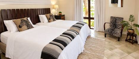 A double bed with striped bedding, a nightstand with a lamp, a zebra-patterned chair, and a view of the outdoors through a glass door.