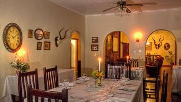 A dining area with tables set for two, a ceiling fan, and wall-mounted clocks.