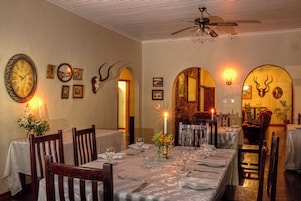 Un comedor con mesas dispuestas para dos, un ventilador de techo y relojes en la pared.