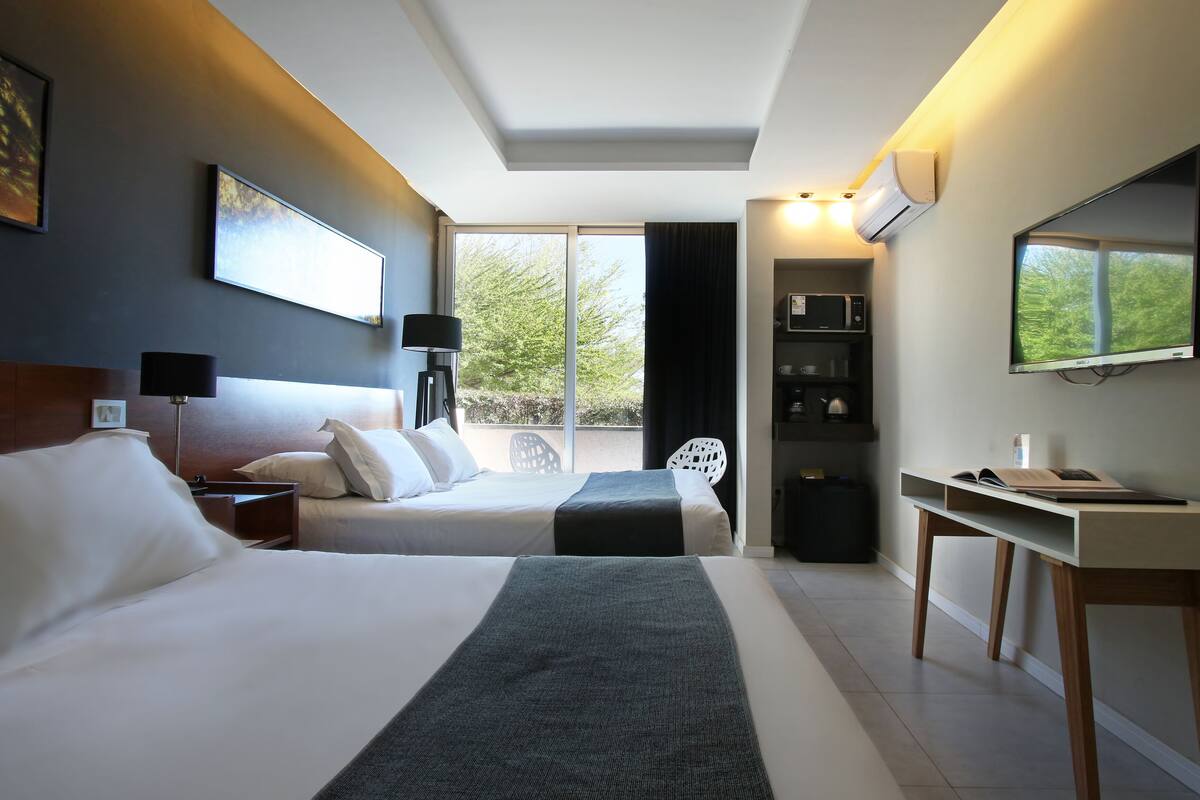 Ett hotellrum med två sängar, ett skrivbord, en stol, en platt-TV och ett fönster med utsikt över träd.