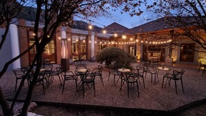 Une terrasse extérieure dotée de plusieurs tables et chaises, entourée de murs en briques et illuminée de guirlandes lumineuses.