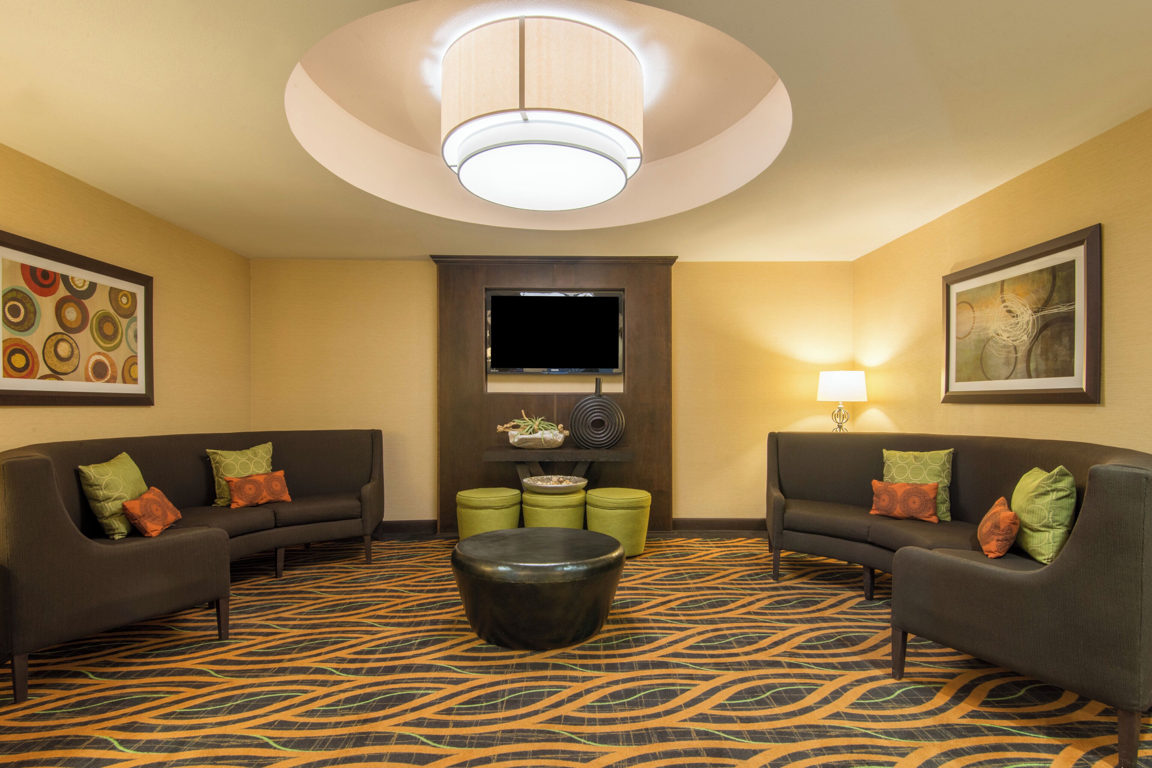 A hotel room with two sofas, a coffee table, a flat-screen TV, and artwork on the walls.