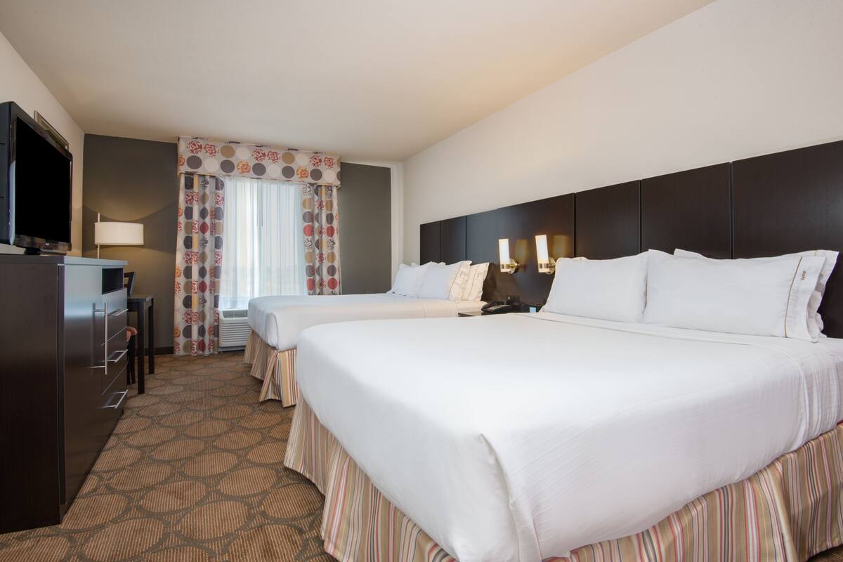 A hotel room with two beds, a TV, a desk, and a lamp.