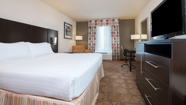 A hotel room with a large bed, a flat-screen TV, a desk, and a chair.