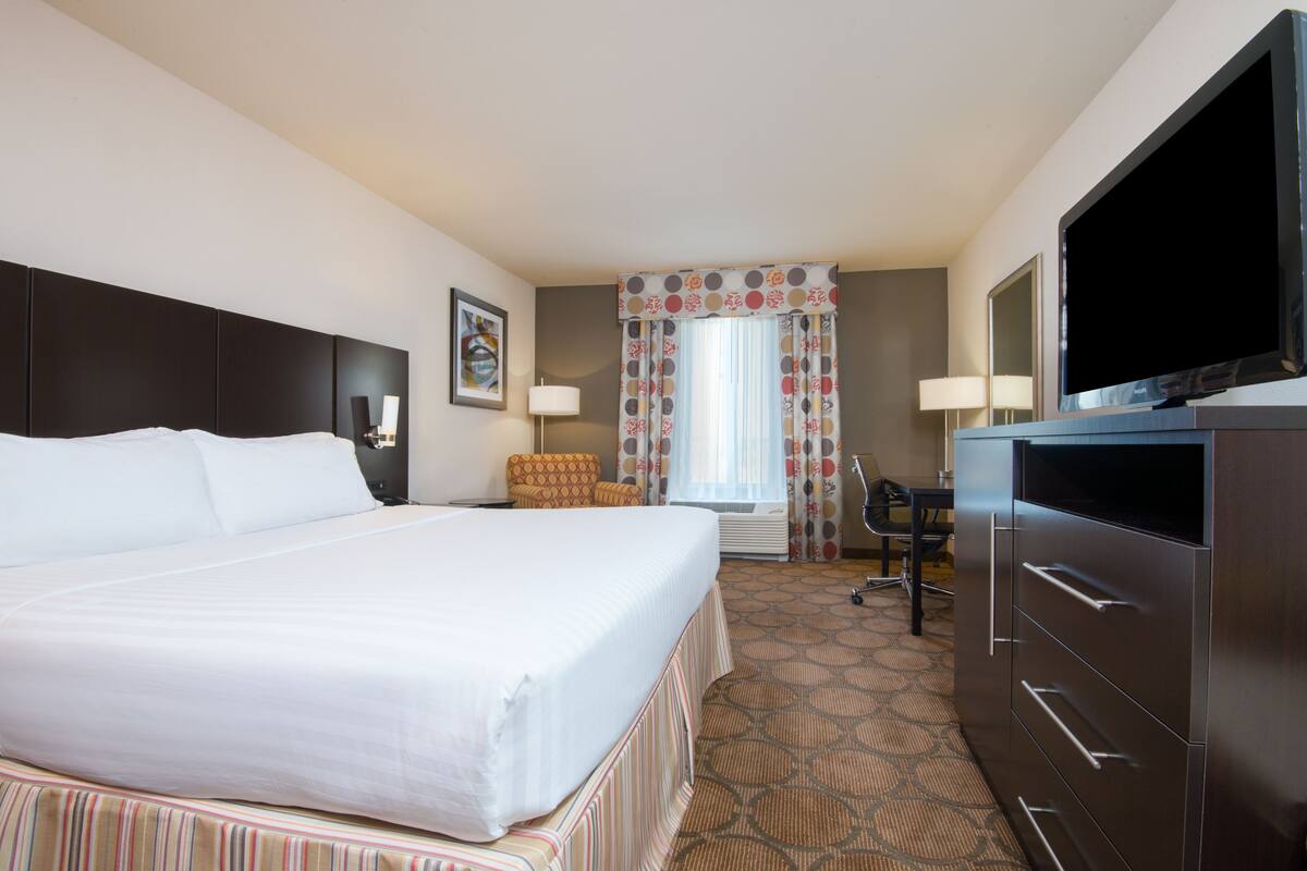 A hotel room with a large bed, a flat-screen TV, a desk, and a chair.