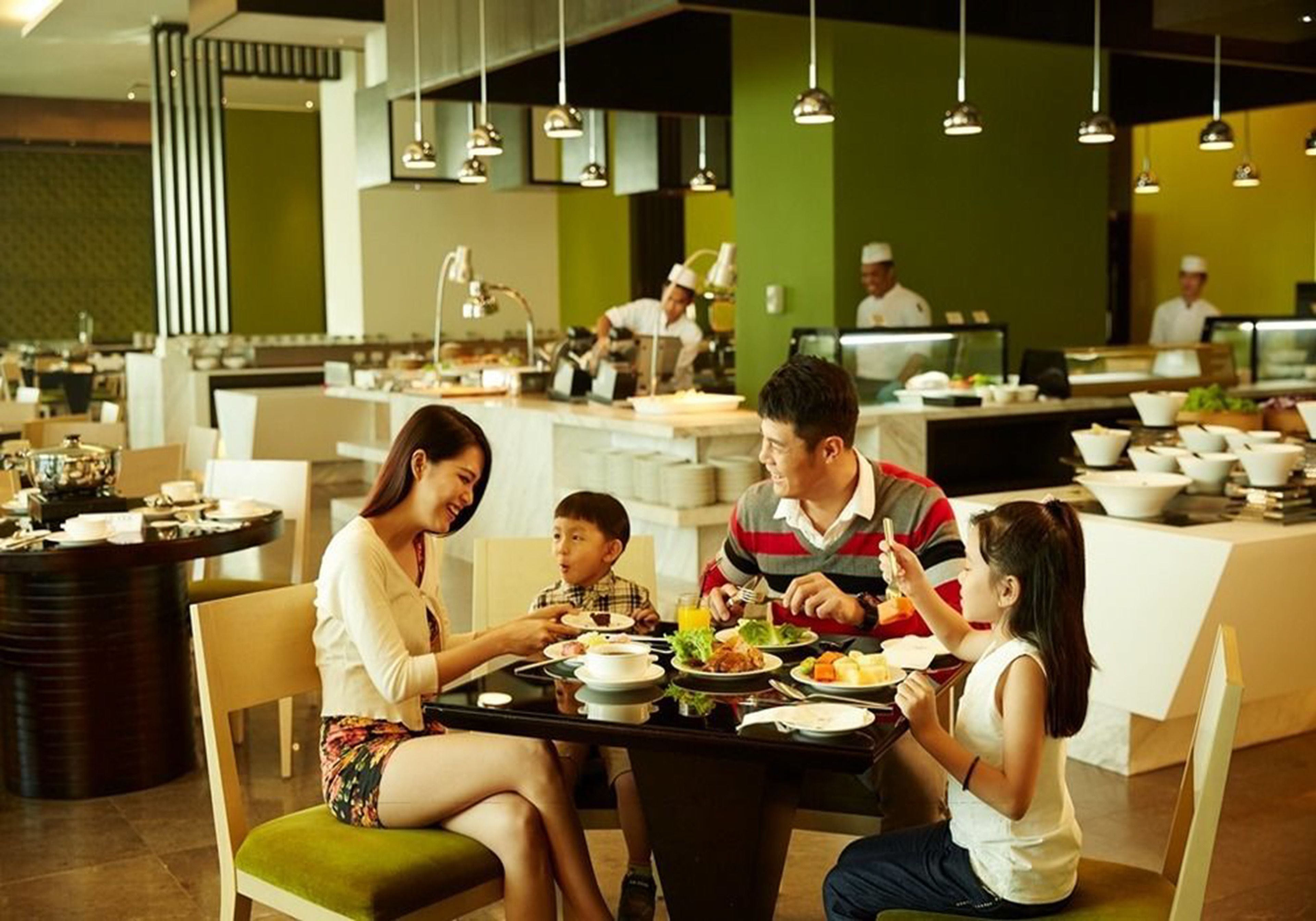 A family dining at a restaurant with a modern interior, including a central dining table surrounded by chairs, and a kitchen area in the background.