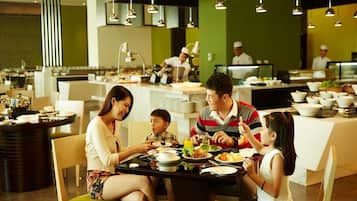 A family dining at a restaurant with a modern interior, including a central dining table surrounded by chairs, and a kitchen area in the background.