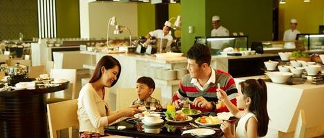Una familia cenando en un restaurante con una decoración moderna, que incluye una mesa central rodeada de sillas y una zona de cocina al fondo.
