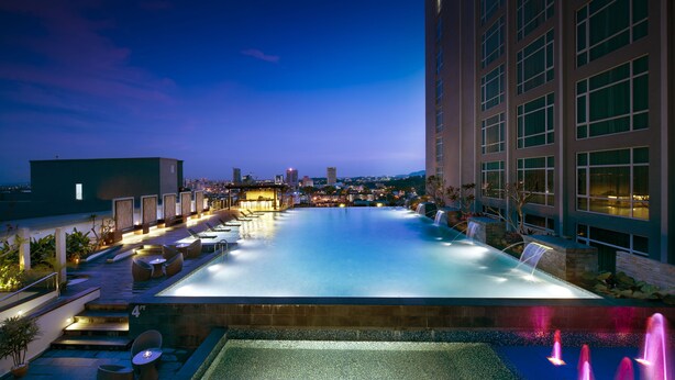 Zona de piscina en la azotea con vistas al horizonte de la ciudad al anochecer.