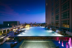 Zona de piscina en la azotea con vistas al horizonte de la ciudad al anochecer.