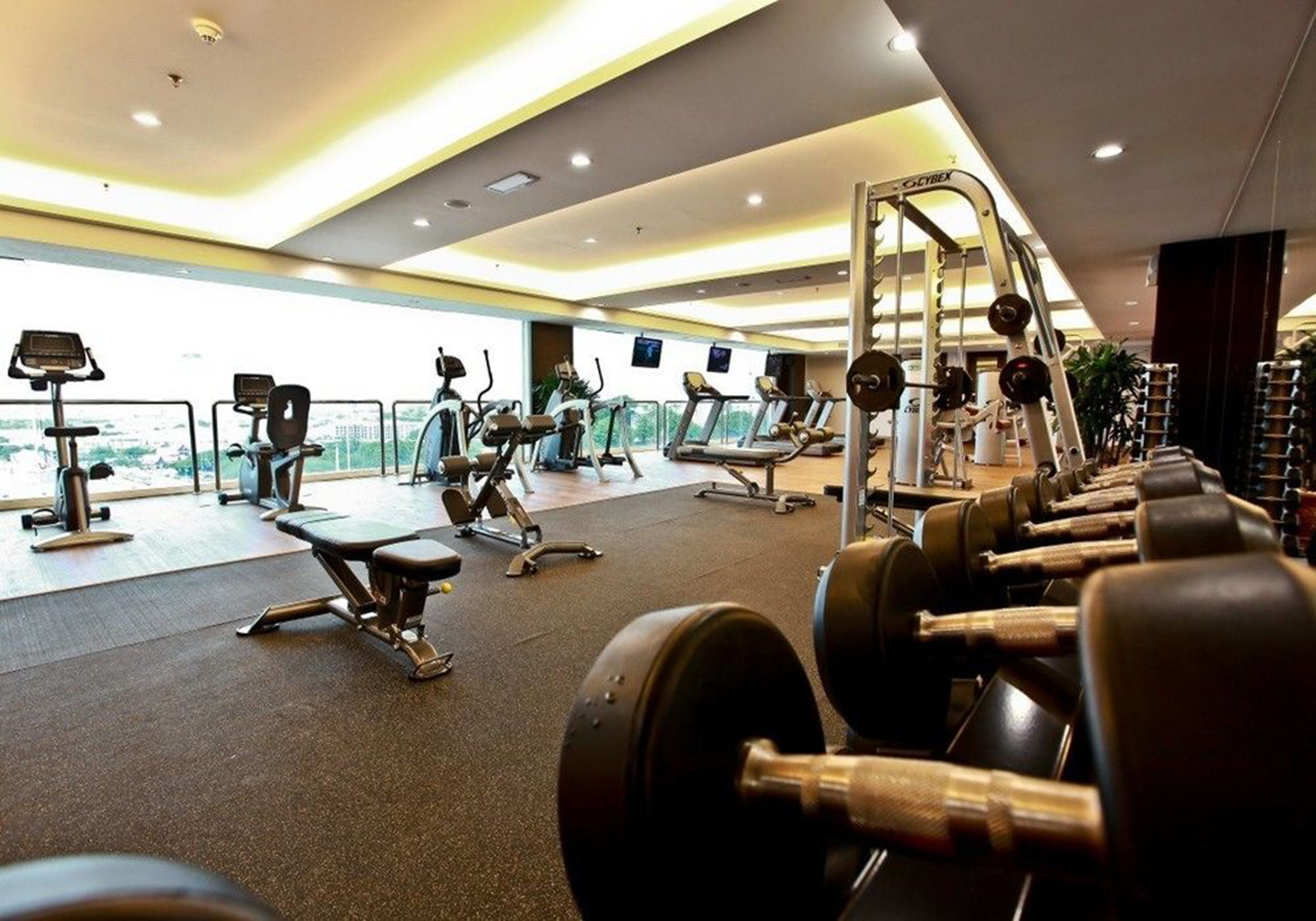Une salle de sport équipée de machines de cardio, de matériel de musculation et offrant une vue sur la ville.