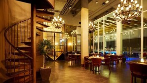 Un restaurante de varios niveles con una escalera de madera, varias mesas para comer y candelabros.