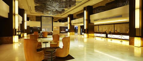 A spacious lobby with a high ceiling, modern chandeliers, and a reception desk.