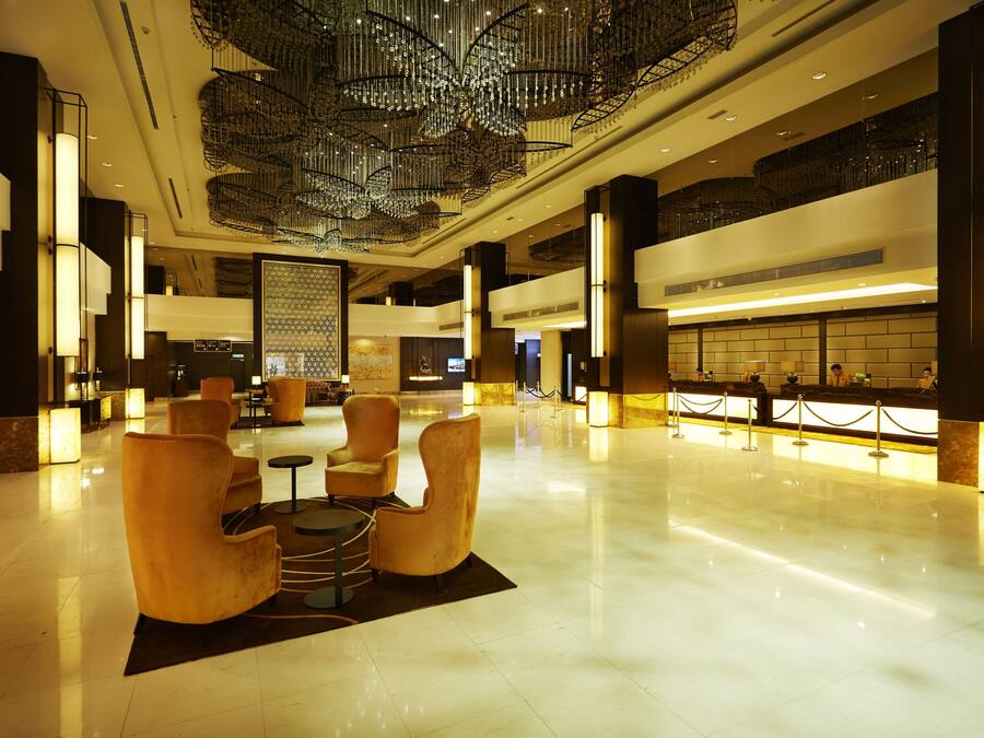 A spacious lobby with a high ceiling, modern chandeliers, and a reception desk.