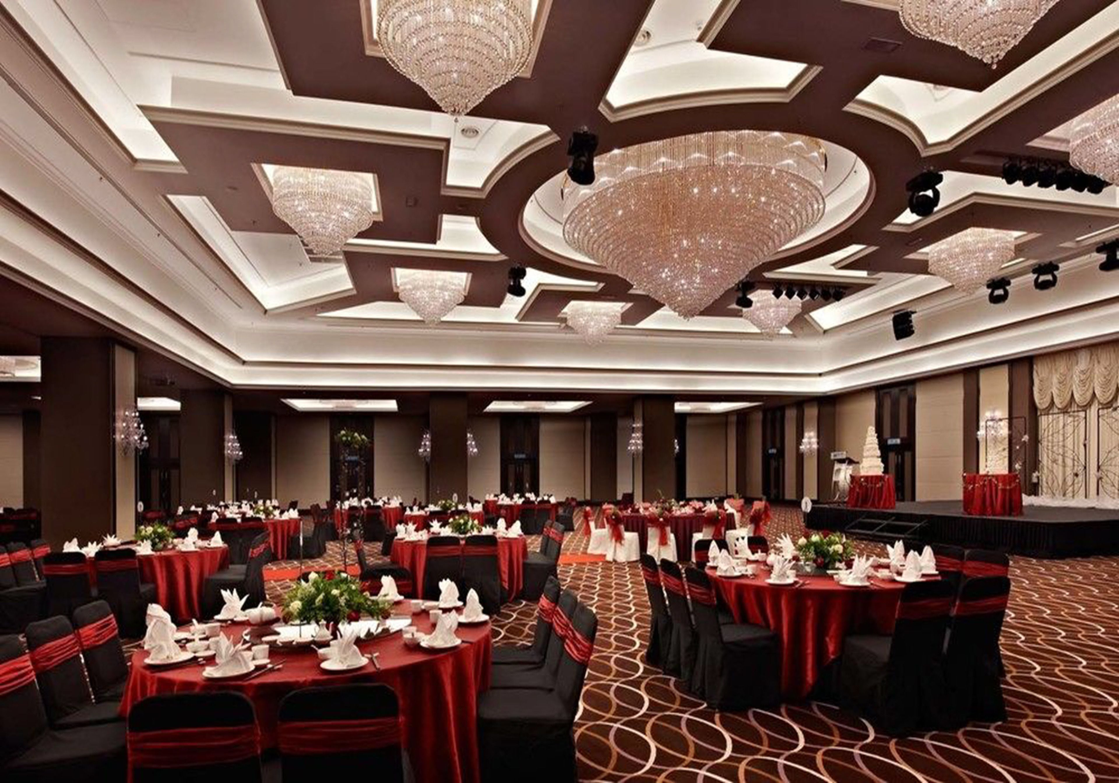 A banquet hall with round tables, red tablecloths, and black chairs.